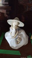 Front and slight angle view of Lladro porcelain figurine showing girl sitting with large hat and basket of flowers.