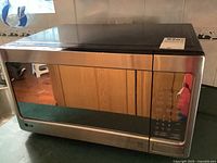 Front view of LG stainless steel microwave oven on kitchen countertop with reflective glass door and digital control panel visible.