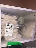 Multiple quilting fabric kits stacked and sealed in plastic bags on a shelf.