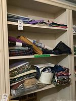 Three shelves with multiple folded and rolled quilting fabrics and blocks, various colors and patterns visible