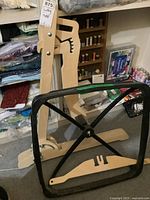 Photo of a wooden and black metal quilting frame standing upright with adjustable wooden parts, set in a sewing room with fabric and sewing supplies visible.