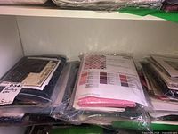 Quilting kits sealed in plastic bags on a shelf, containing fabric and pattern sheets.