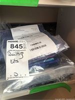 Photo of quilting kits in clear plastic bags with packing label and handwritten markings, showing contents packed together.