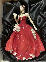 Front view of the Royal Doulton Happy Birthday 2008 figurine, showing the lady in red dress holding a card, with floral details and black satin background.