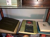 Three stamp albums and presentation sets displayed on shelf, including the Official Presentation Sets of the International Society of Postmasters 1981 and Canada stamp albums.