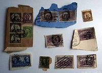 Photo of fourteen vintage USA stamps including six 1892 Columbus Commemorative two cent stamps with fancy cancels and assorted other vintage stamps affixed to pieces of paper.
