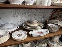 Shelf view showing multiple pieces of antique Tudor Rose china including plates, oval serving trays, and a covered serving dish with floral patterns.