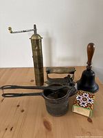 Photo showing all five items in the lot: brass coffee grinder, metal masher, vintage iron, cast iron hand bell, and beaded match box cover with vintage match box.