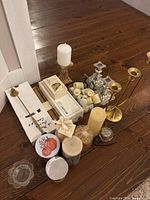 Photo showing assorted candles and holders arranged on wooden floor