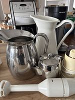 Overview of multiple coffee makers and kitchen items including pitchers, teapot, and emulsifier, on wooden table