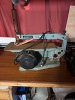 Front side view of Delta 15-inch scroll saw showing the motor on the left, the worktable surface, and the saw arm with Delta branding and specifications.