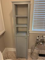 Front view of grey-blue cabinet showing three open shelves above closed cabinet door