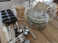Full lot of kitchen items including glassware, cutlery, bakeware, and storage jars on a wooden table