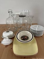 Front view of lot showing jars, plates, butter dishes, Wedgwood Mikado bowl, and vase on wooden table.