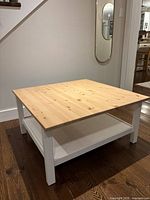 Angled view of the coffee table showing wooden top, white legs, and lower shelf.