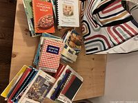 Cookbooks displayed loosely on a wooden table along with a striped tote bag.