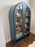Front view of refinished arched display cabinet painted teal-blue with glass-paneled doors and wood mullions