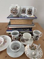 Photo of assorted royal-themed teacups, mugs, plates placed on and around a stack of books
