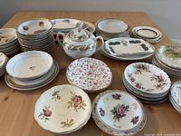 Wide shot showing the full assortment of stacked plates, saucers, and a sugar bowl on the wooden table.