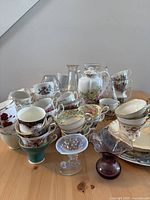Wide view of multiple stacked and displayed teacups, small glass bowls, and vases on wooden table