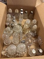 Photo showing all 14 sets of vintage glass salt and pepper shakers inside a cardboard box, displaying various intricate glass patterns and metal caps.