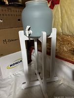 Ceramic water jug on white wooden stand, side view.