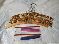 Four padded clothes hangers with floral fabric and gold hooks arranged laid flat. Two unopened and two loose colorful plastic combs from CVS Styling Collection are placed below the hangers on a white surface.