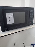 Black Magic Chef microwave oven showing front and digital controls with feature list sticker on door.
