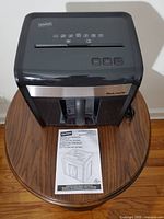 Staples Mailmate bucket shredder with control buttons and instruction manual on wooden table.