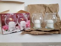 Two clear glass votive candle holders with white votive candles inside, sitting next to their original Cape Cod branded box showing an image of the two holders.
