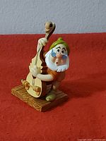 Close-up photo of Doc figurine playing bass violin, showing detailed craftsmanship and colors on a wood-texture base.