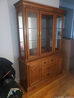 Full view of the wooden china cabinet showing glass hutch with wooden frame doors over buffet base with drawers and doors.