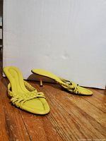 Yellow ladies sandals with woven leather straps and spool heels photographed on floor against white background.