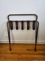 Closed view of collapsible luggage rack showing metal frame and straps horizontally folded