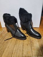 Pair of black ladies snow boots made of imitation leather with faux fur trim and laces, size 10, on wood floor background.