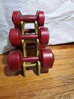 Side view of stacked dumbbells on a yellow plastic rack showing three sets of dumbbells with red plastic coating.