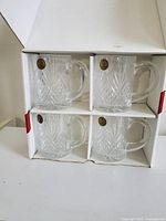Photo of four clear lead crystal mugs with diamond cut design in white cardboard box with dividers