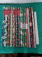 29 rolls of gift wrapping paper laid out on a green surface, showing a variety of Christmas, wedding, children and general occasion patterns.