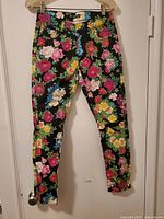 Front view of floral print jeans hanging on door, showing vibrant spring flower pattern on black background and slim fit.