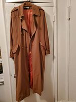 Full front view of the camel colored woolen overcoat hanging, showing the gold buttons and the satin lining inside the coat.