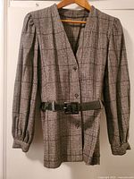 Front view of woman's plaid blazer showing button cuff sleeves, V-neck, and black patent leather belt at the waist.