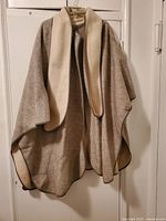 Front view of the reversible women's winter cape showing the gray side with attached cream scarf.