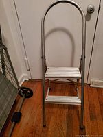 Photo of the metal 2-step ladder showing the side view with handgrip and rubber feet on wooden floor.