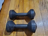 Two vintage 10-lb iron dumbbells placed on a wooden floor, showing their hexagonal ends and rugged vintage condition.