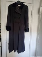 Full view of the black dress coat hanging on a hanger showing front double-breasted design with velvet collar and cuffs