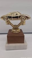 Front view of gold Porsche car trophy on wood and marble base