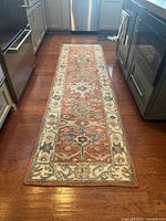One of the Pottery Barn Channing Persian-style runners placed in a kitchen between cabinets and dishwasher, showing the red base color with floral and geometric patterns and beige border.