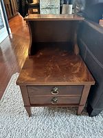 View of the side table showing top surface, curved side panels, two drawers with metal ring pulls, and wood finish.