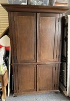Closed dark wooden armoire with four paneled doors showing front view.