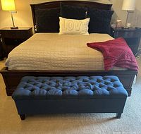 The bench positioned in front of a bed, showing the tufted fabric upholstery and dark blue color.
